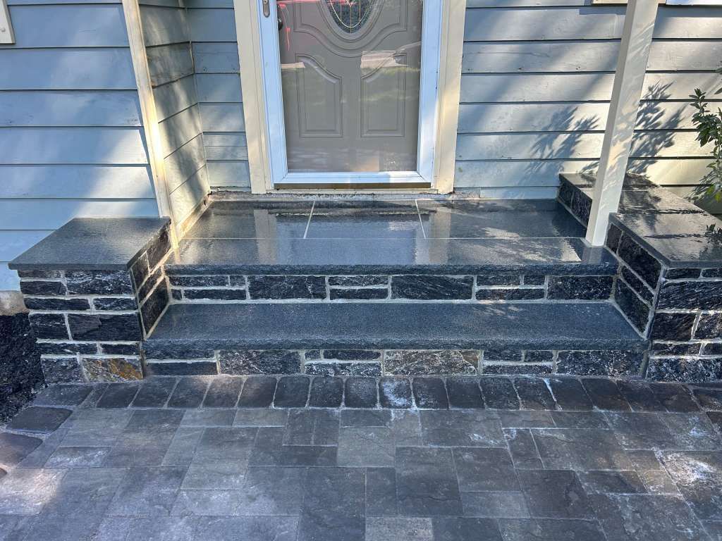 Front porch with dark stone steps and white siding, leading to a gray front door.
