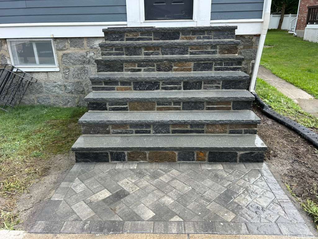 Front steps to a house with dark stone risers and a light patterned paver landing.