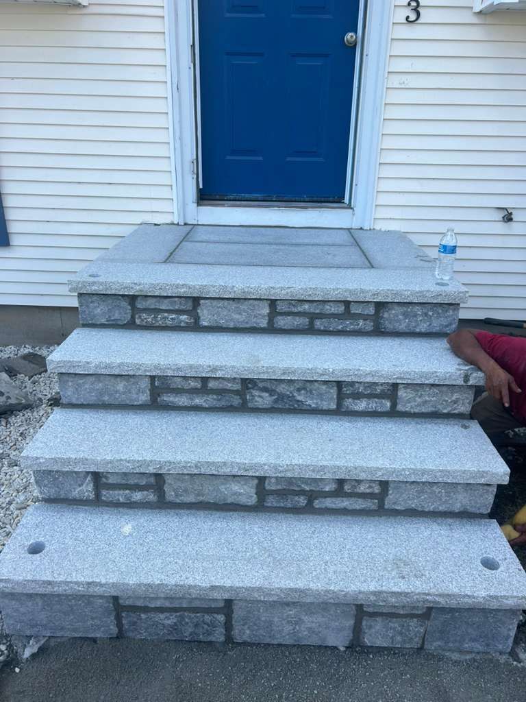 Front steps of a house with blue door and gray stone stairs leading up to the entrance.
