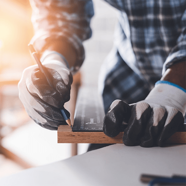 A man is measuring a piece of wood with a ruler and pencil.