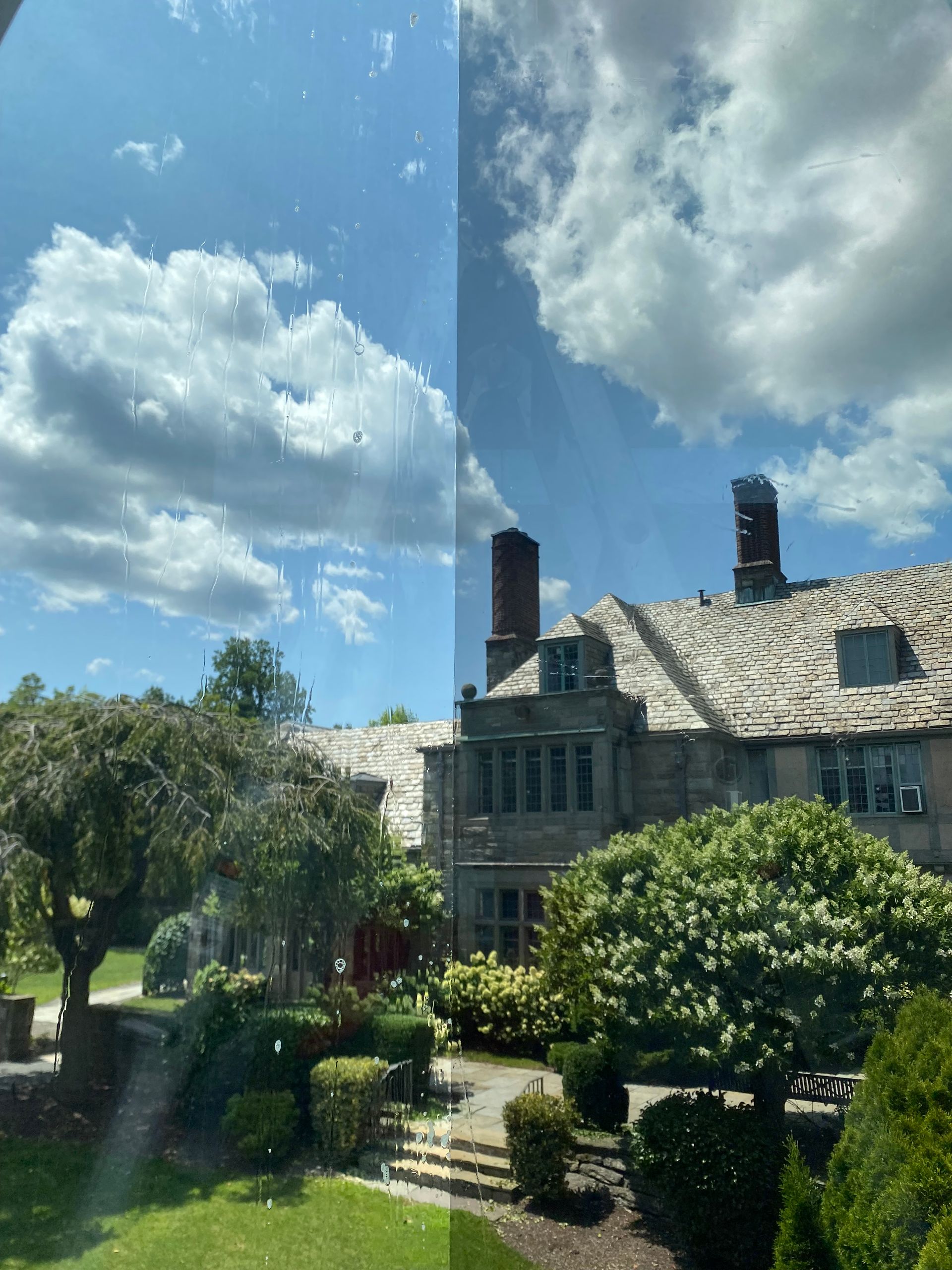 A house with a tiled roof is surrounded by trees and bushes on a sunny day.