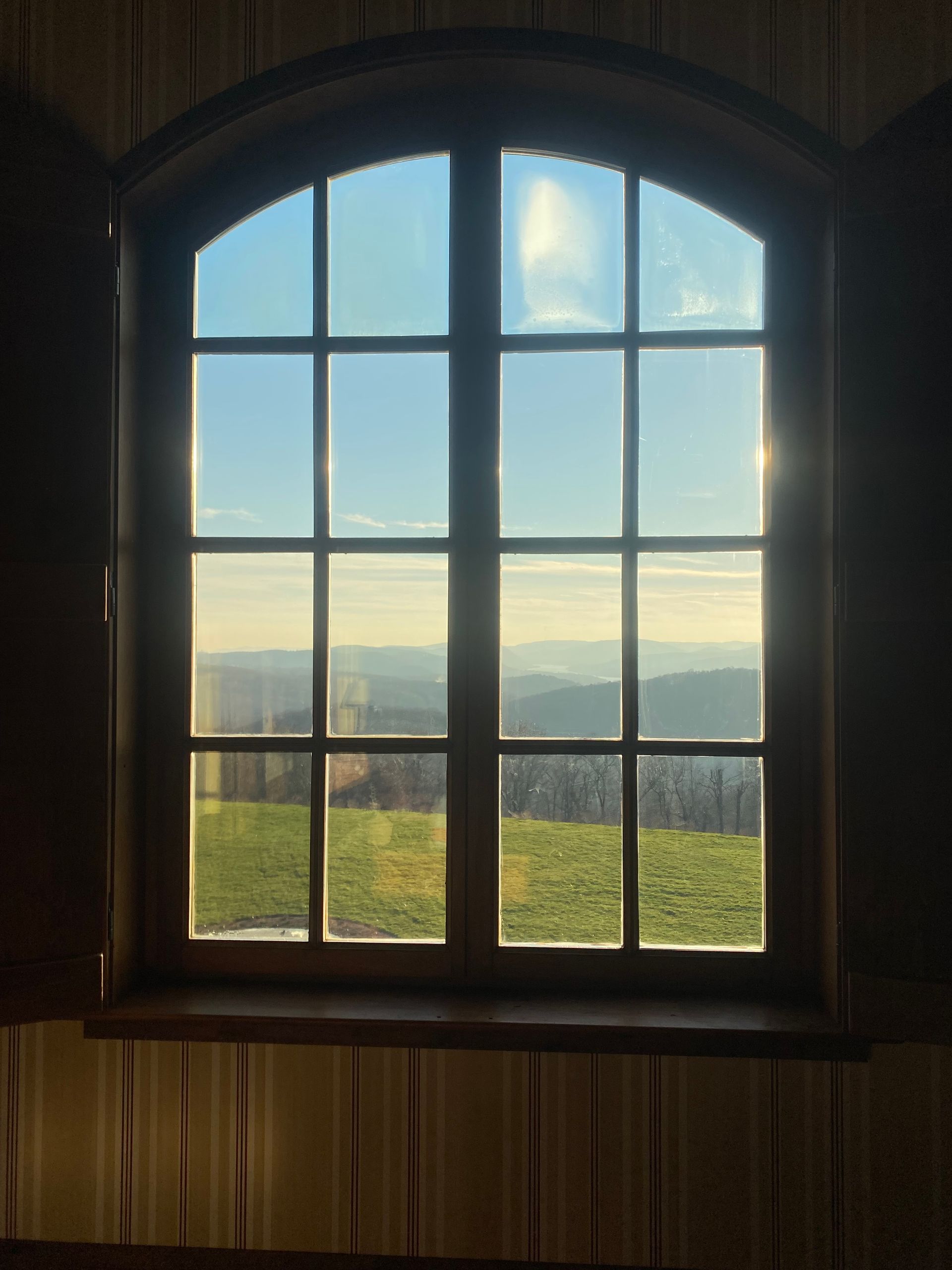 The sun is shining through a window with a view of a field.