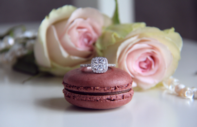 Rose pink macaron with a diamond ring, flanked by pale pink roses on a soft white surface