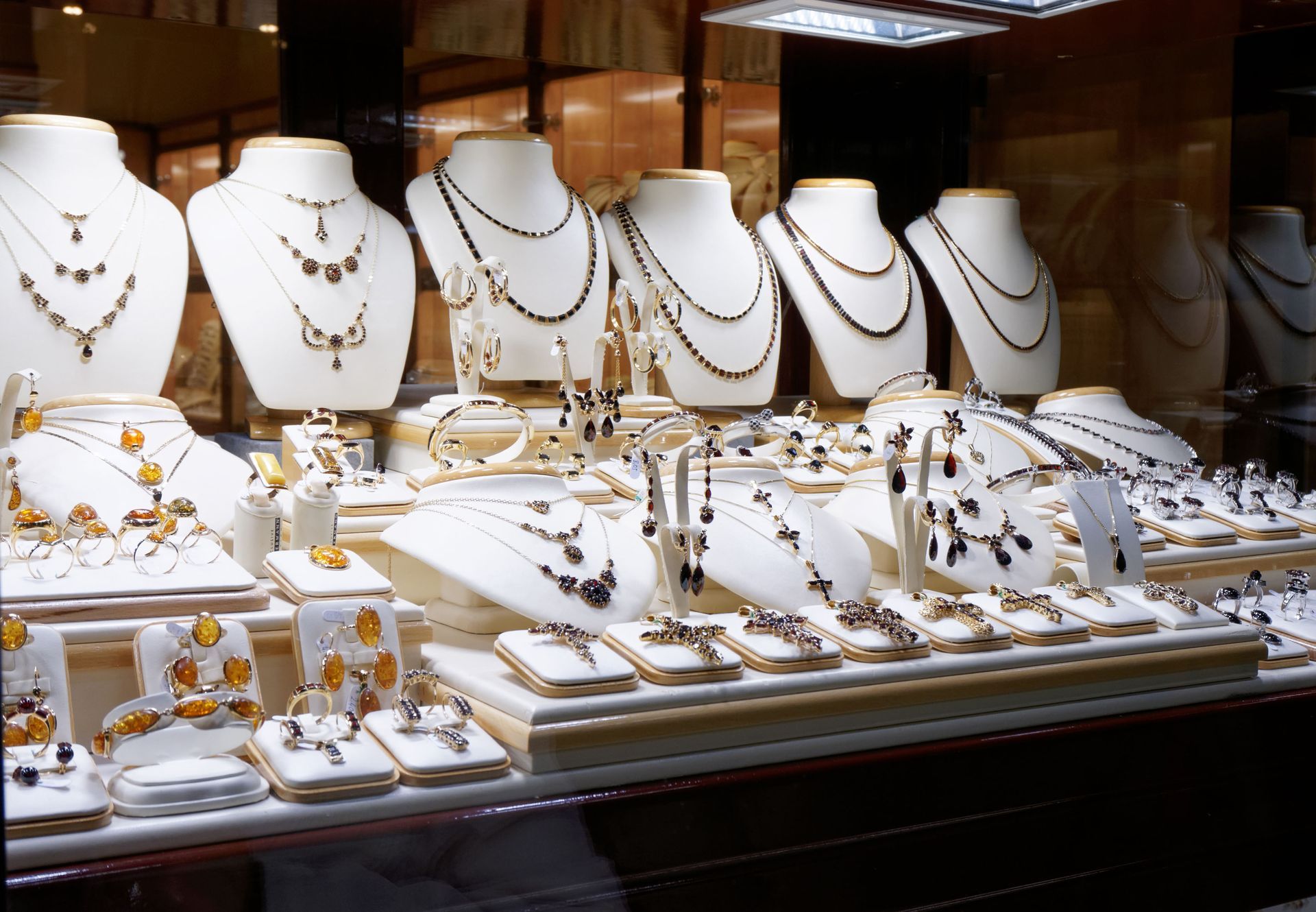 Jewelry display case with necklaces, bracelets, and earrings on white busts and platforms.