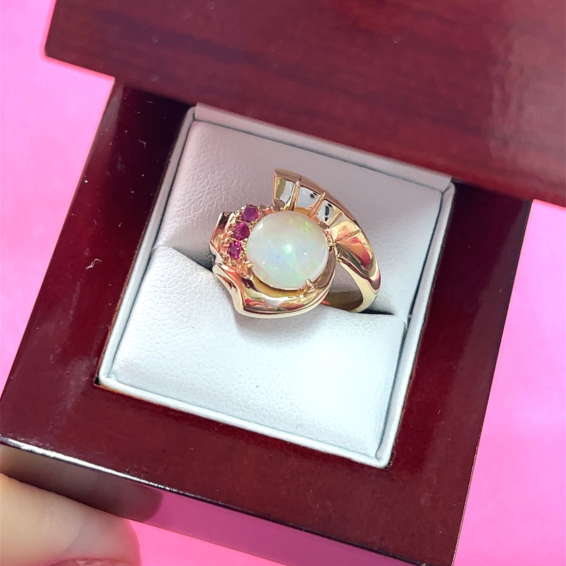 Gold ring with large opal and red gemstones in a wooden box.