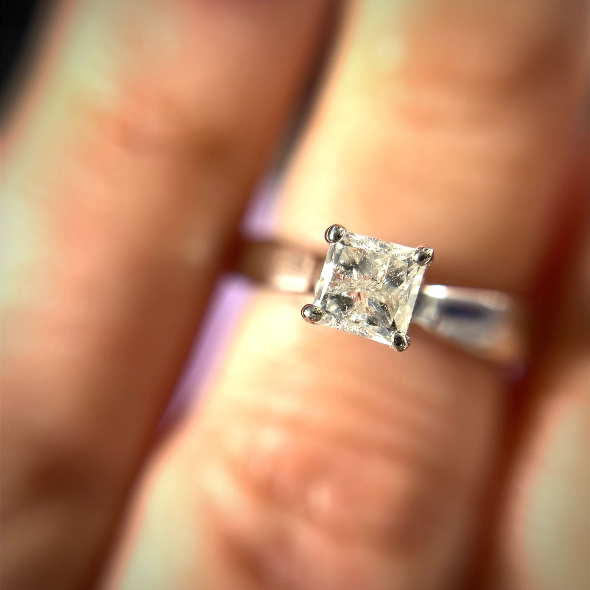 Diamond engagement ring on a finger. The ring has a square-cut diamond set in a silver band.