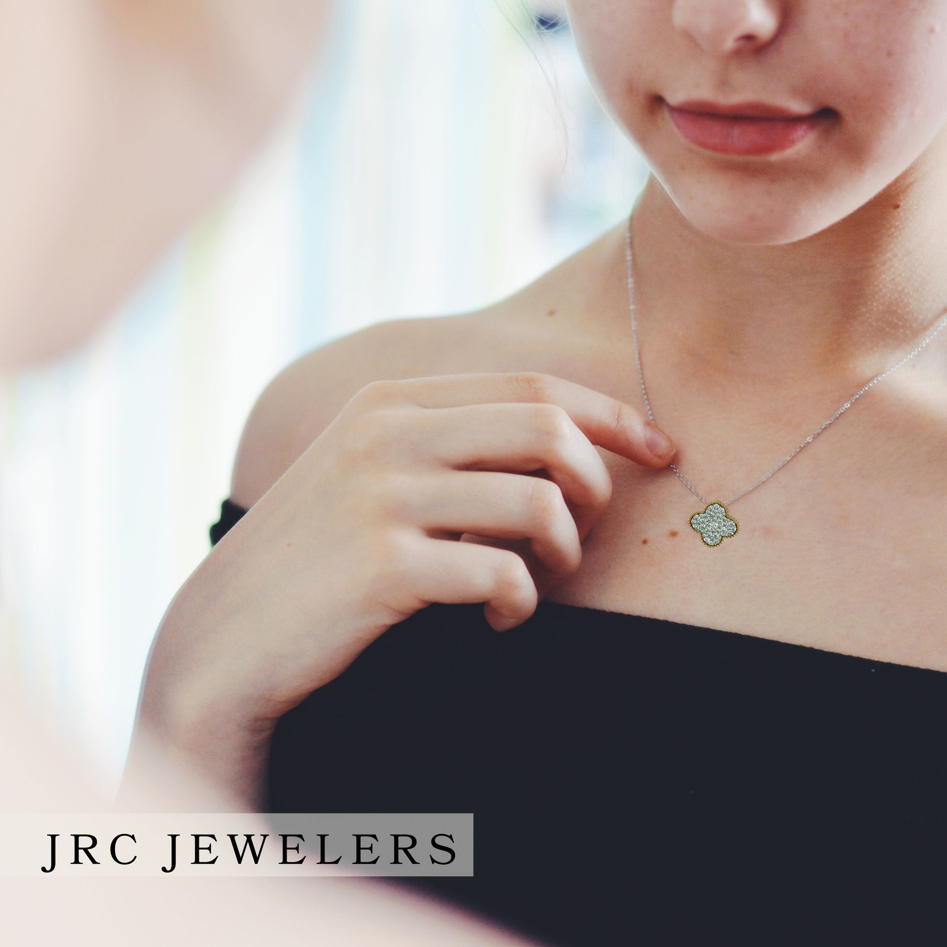 Woman in black top admiring a silver necklace with a square pendant; JRC Jewelers logo.