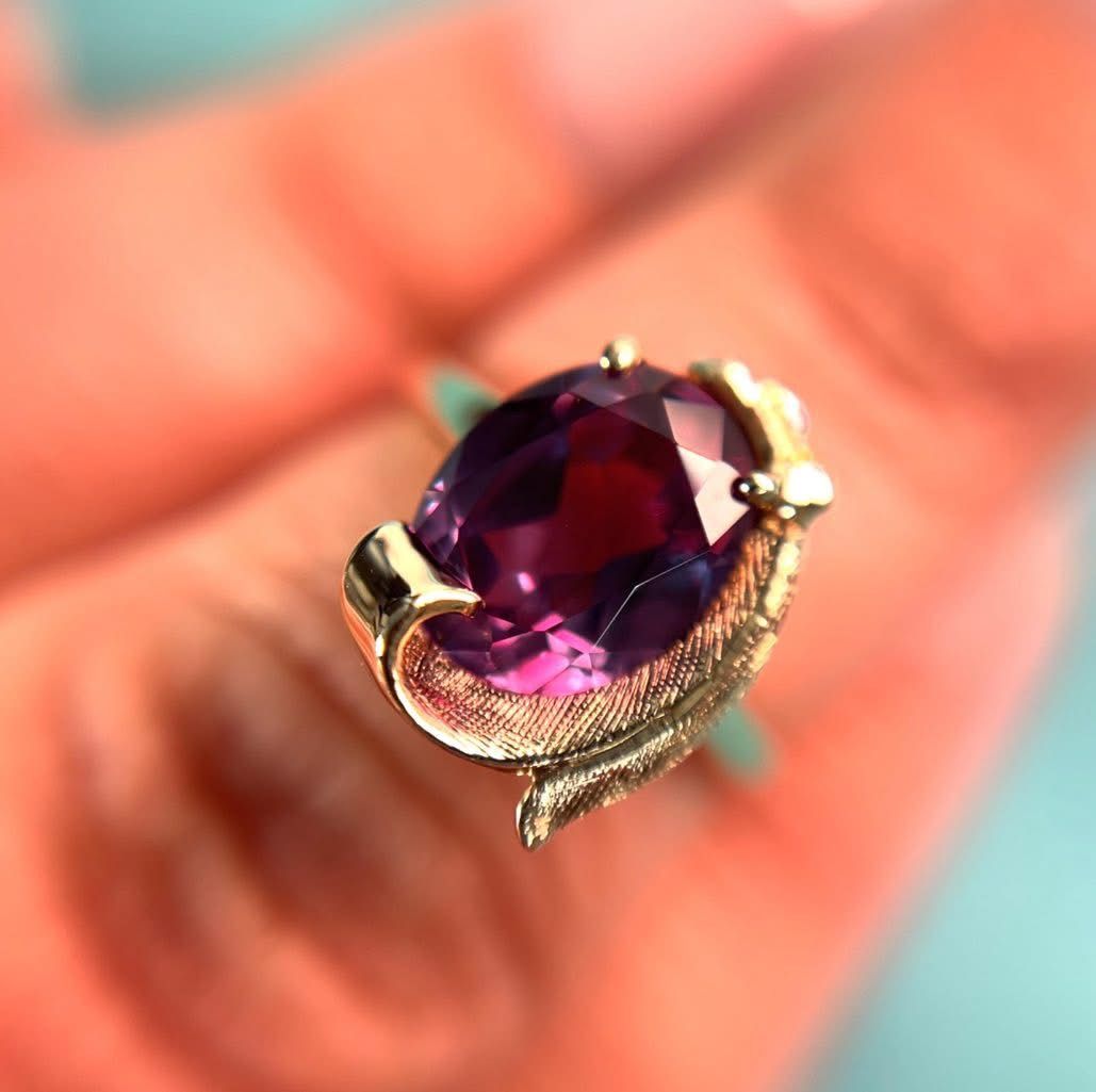 Gold ring with a large, oval, color-changing alexandrite gemstone, held by a hand.