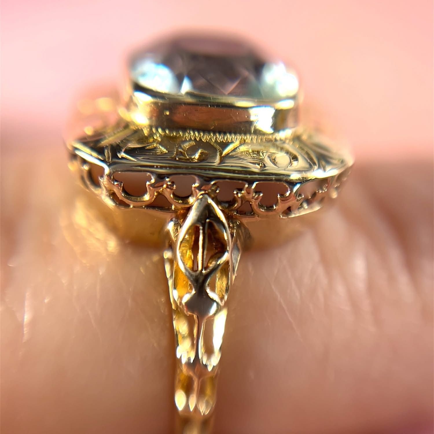Gold ring with a large, oval gemstone, ornate filigree details, on a wrist.