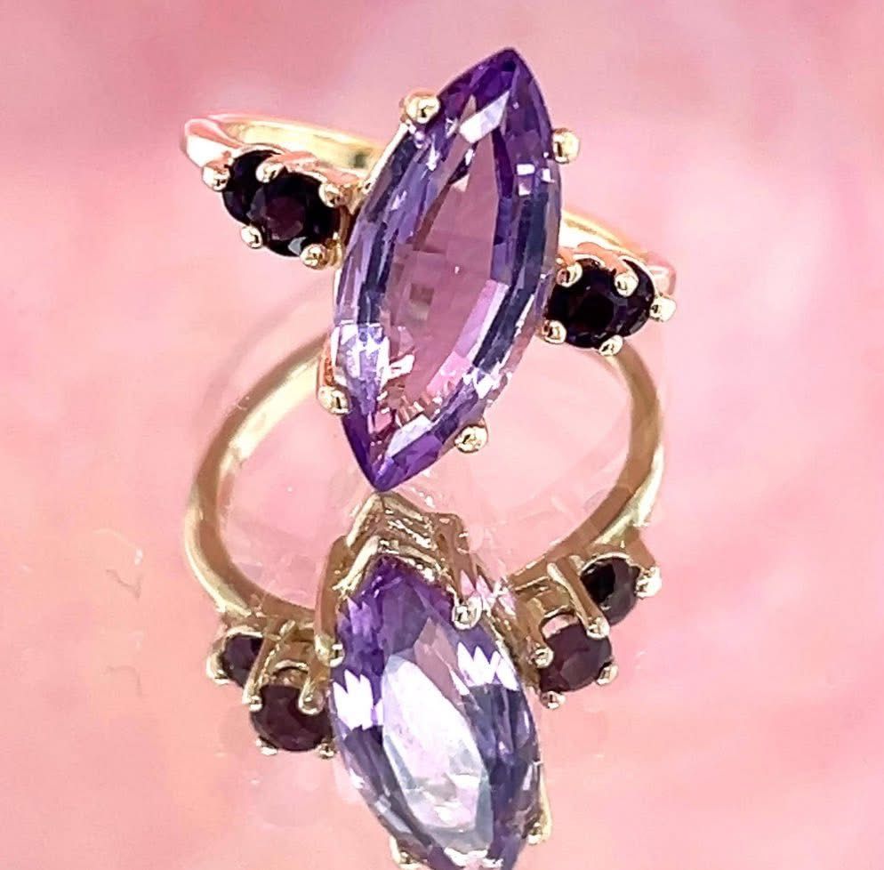 Gold ring with a large, purple marquise-cut stone and smaller, dark gemstones on either side.