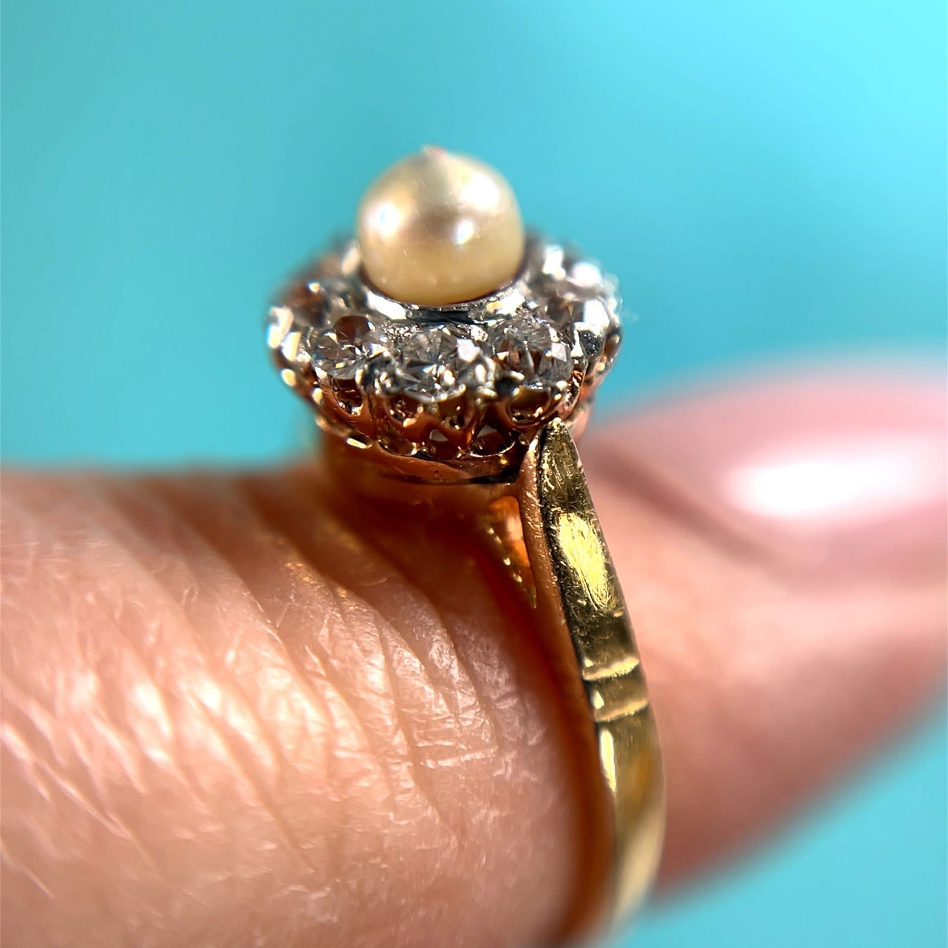 Gold ring with a pearl center stone and surrounding diamonds, held on a finger.