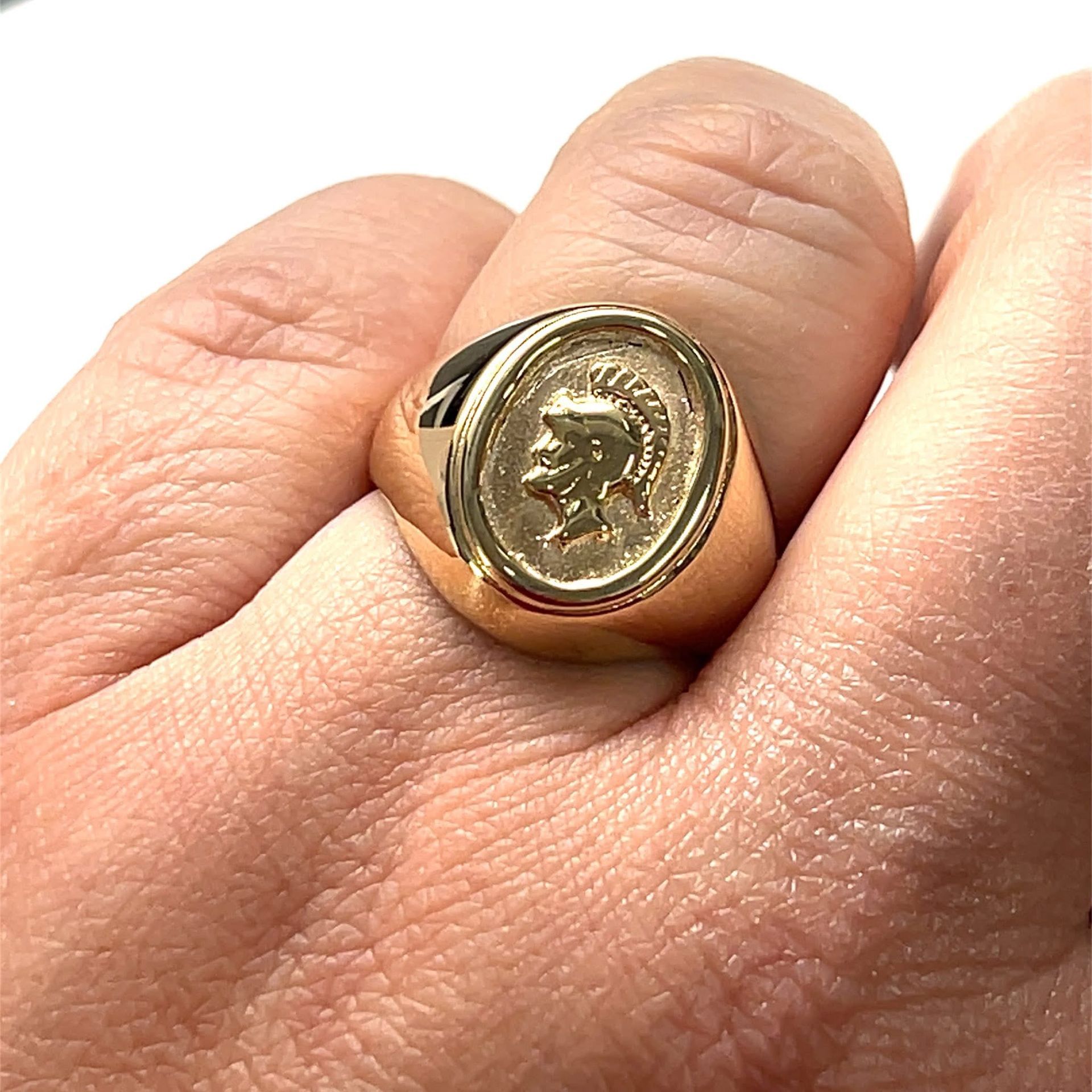 Gold ring with oval face, showing a side profile, worn on a finger.