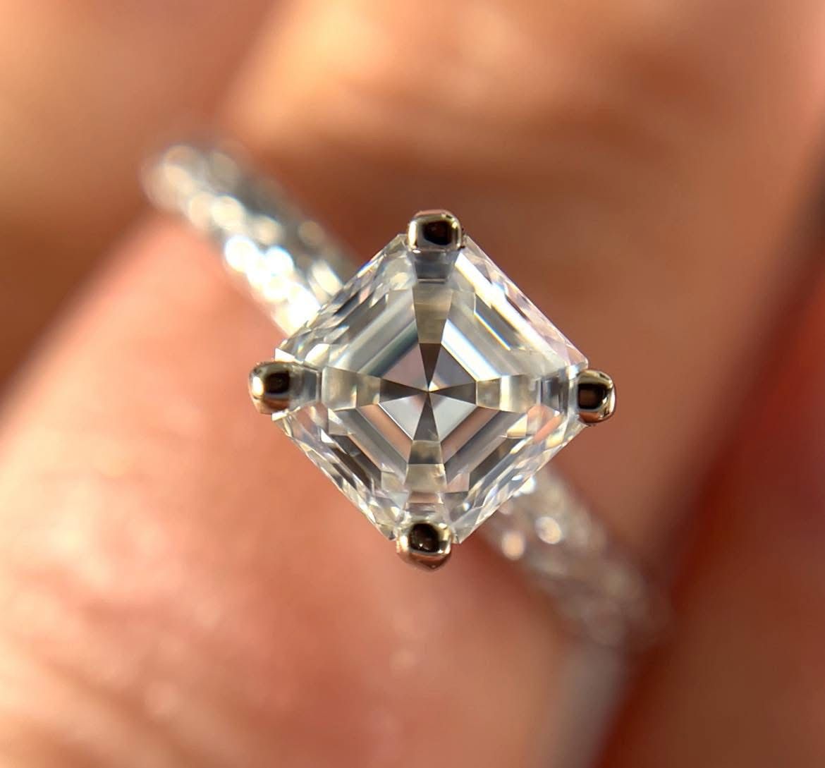Square-cut diamond ring with a textured silver band, held by a hand.
