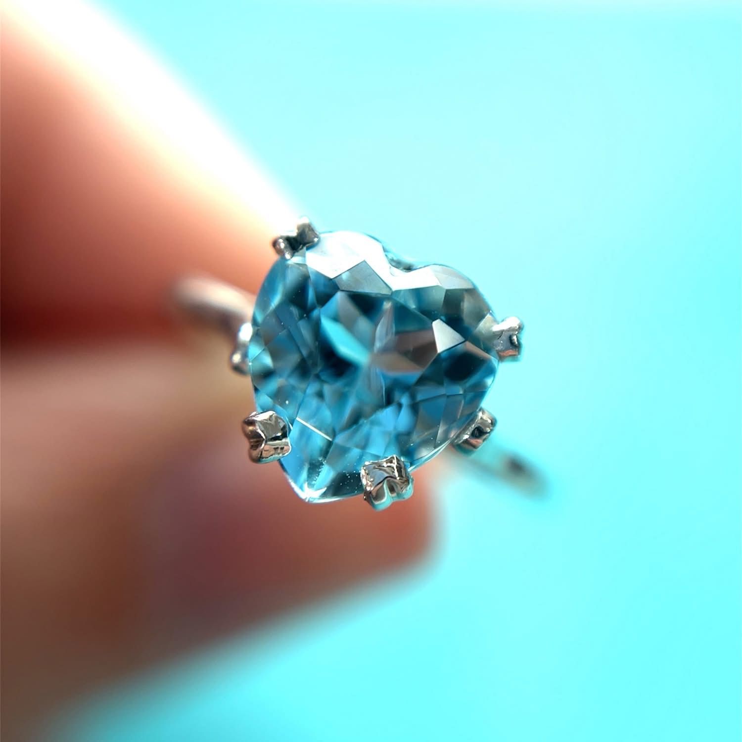 Heart-shaped blue gemstone ring held against a light blue background.
