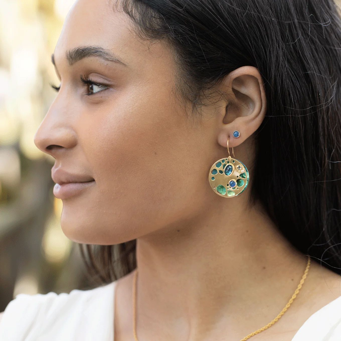 Woman wearing gold earrings with blue and green stones, looking away.
