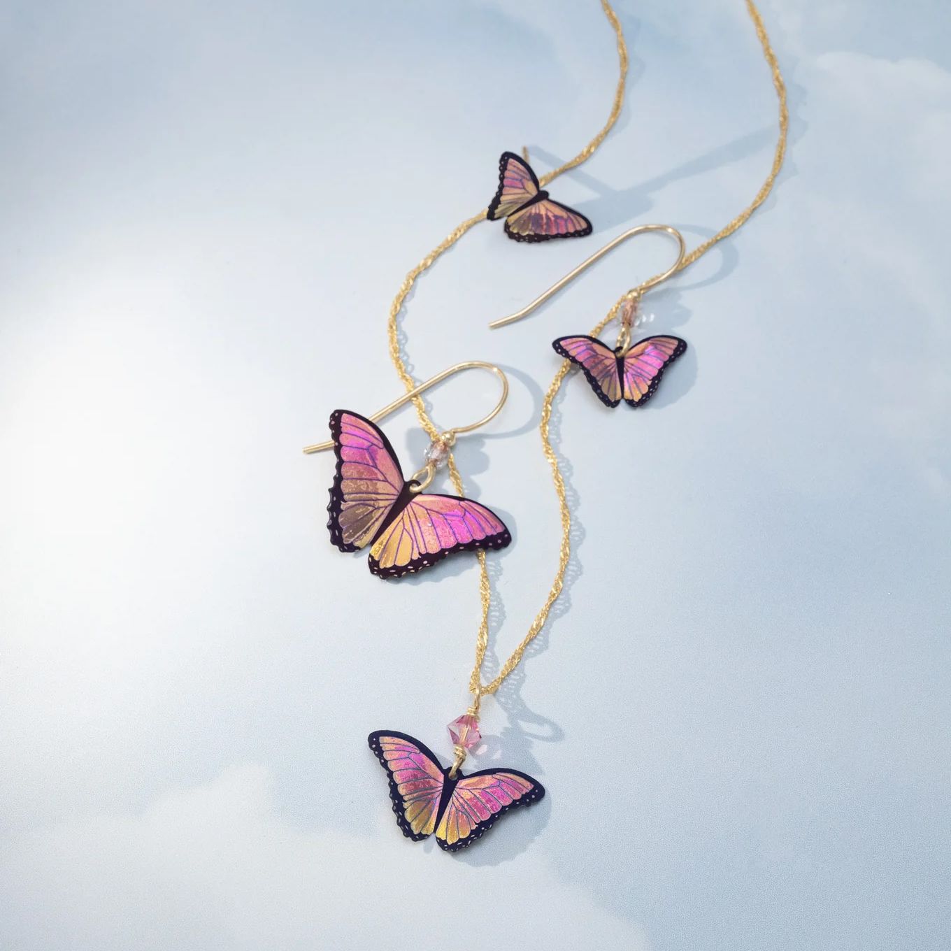Golden necklace and earrings with pink and purple iridescent butterfly charms.