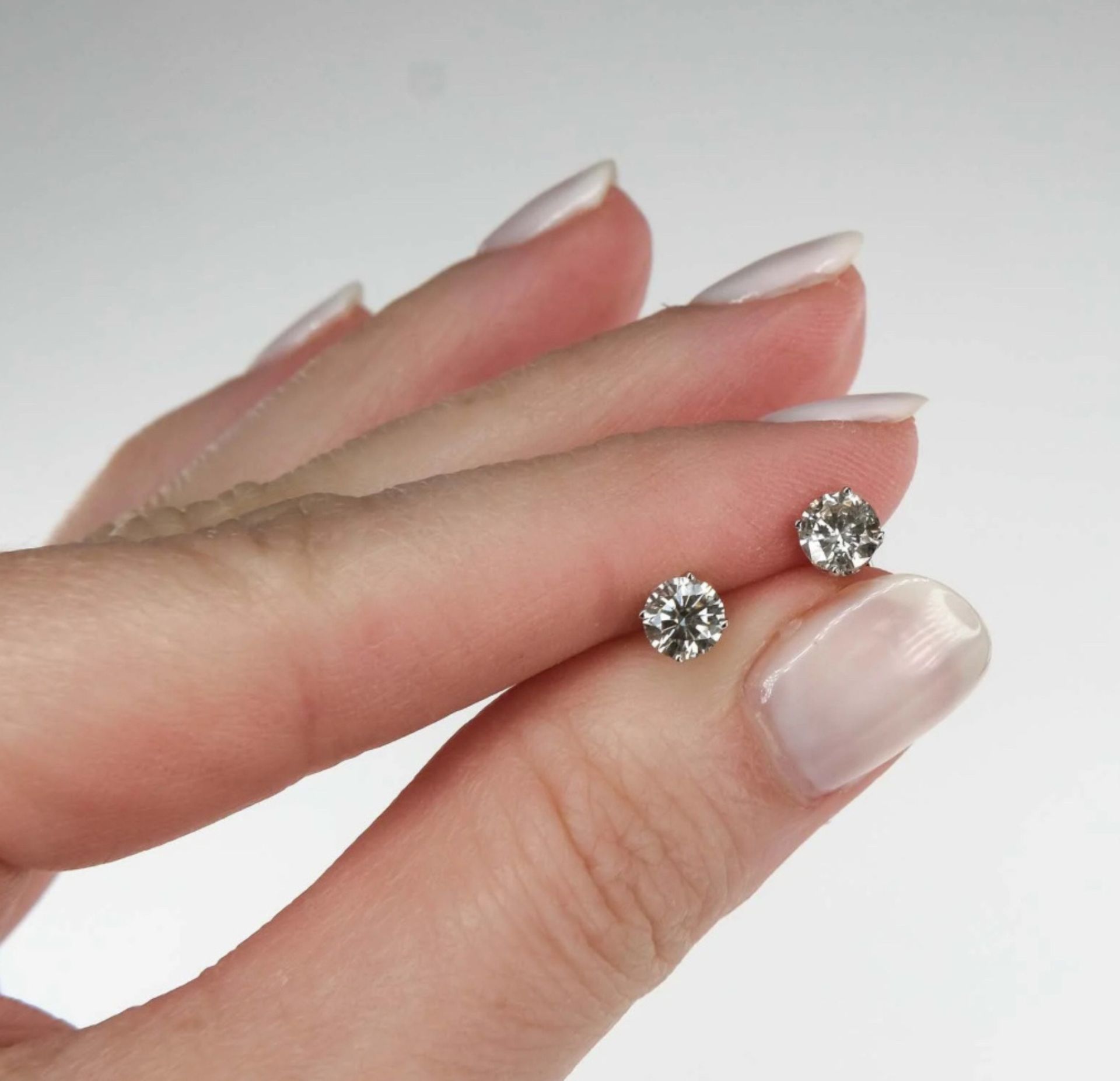 Hand holding a pair of clear, round stud earrings with light reflecting off the stones.