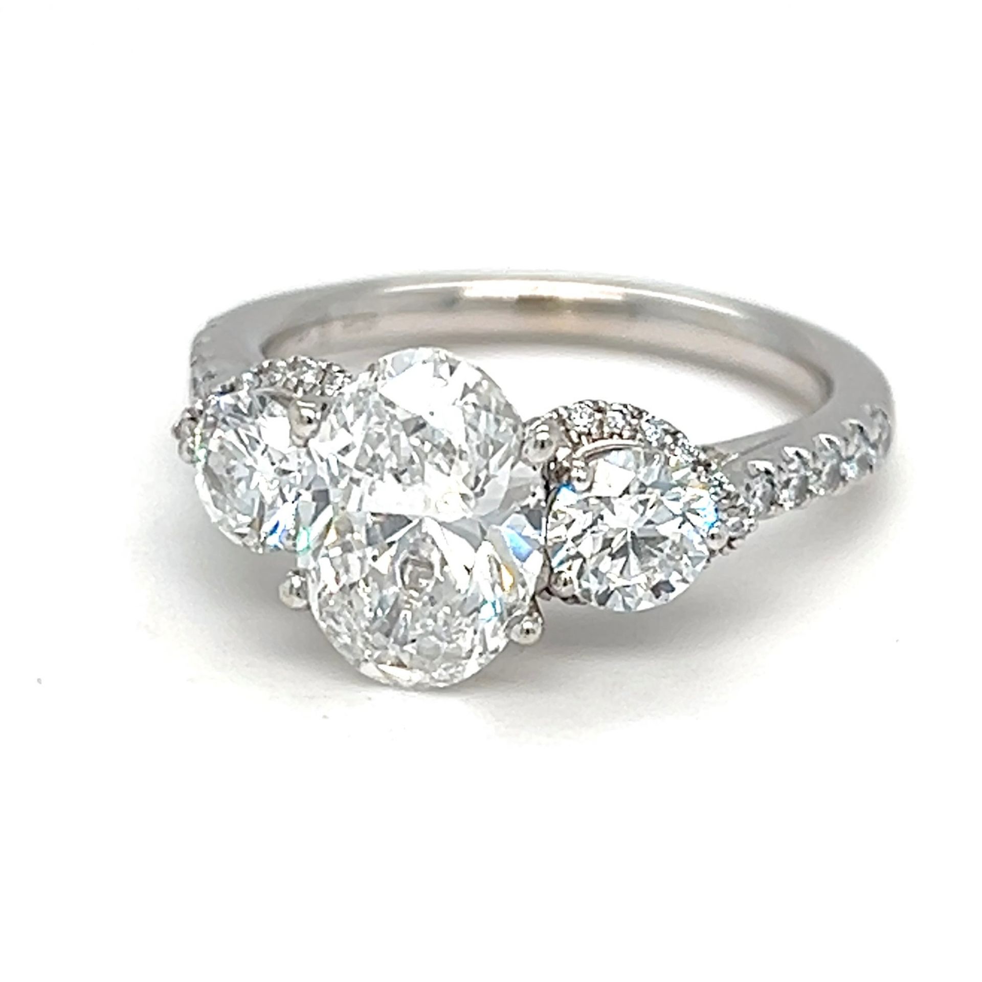 Three-stone diamond engagement ring with an oval center stone and smaller round side stones, set in a silver band.
