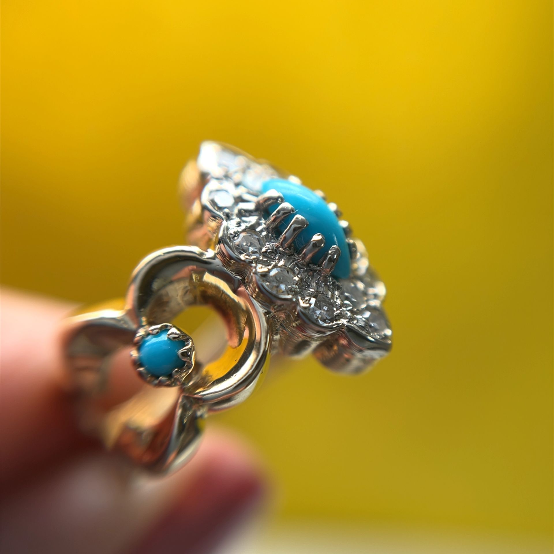 Gold ring with turquoise and diamond accents on a yellow background.