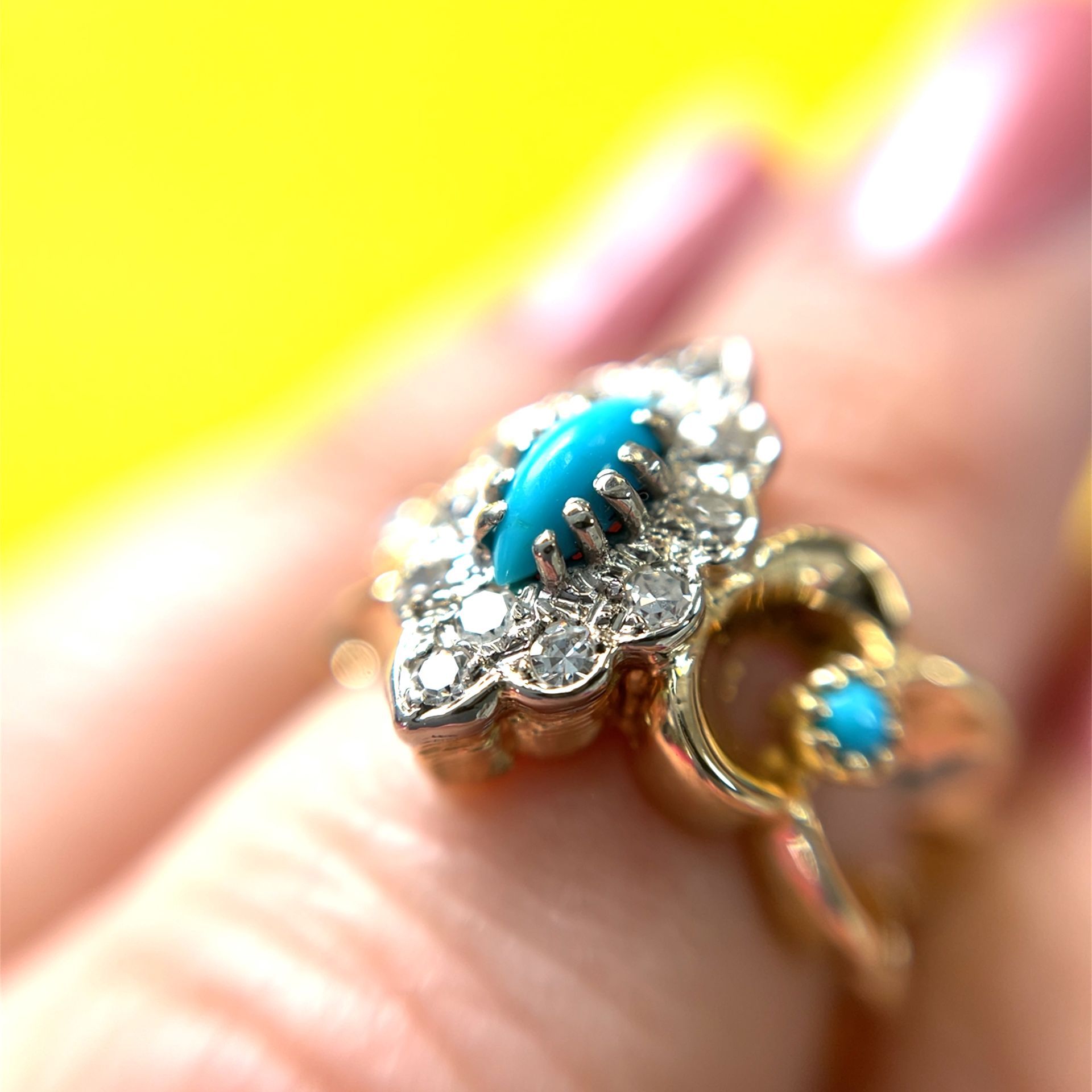 Gold ring with turquoise and diamond accents, worn on a finger.