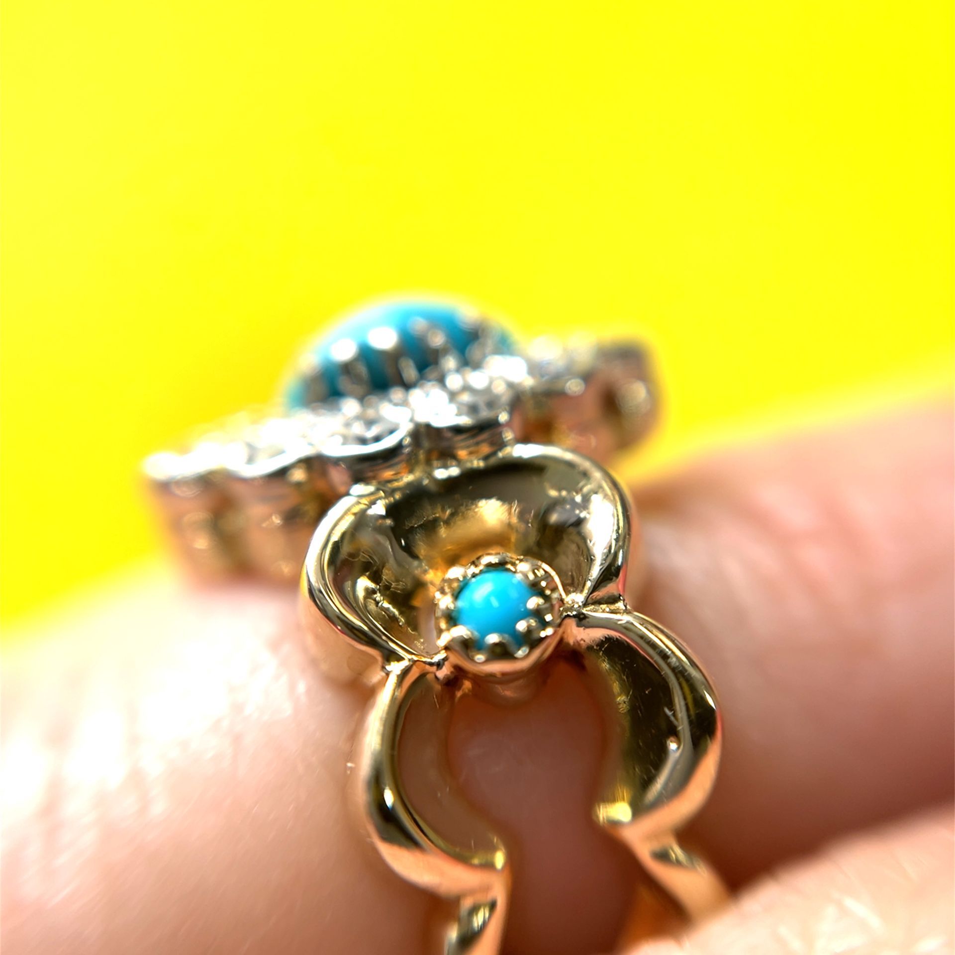 Close-up of two gold rings with turquoise stones and floral designs, against a yellow background.