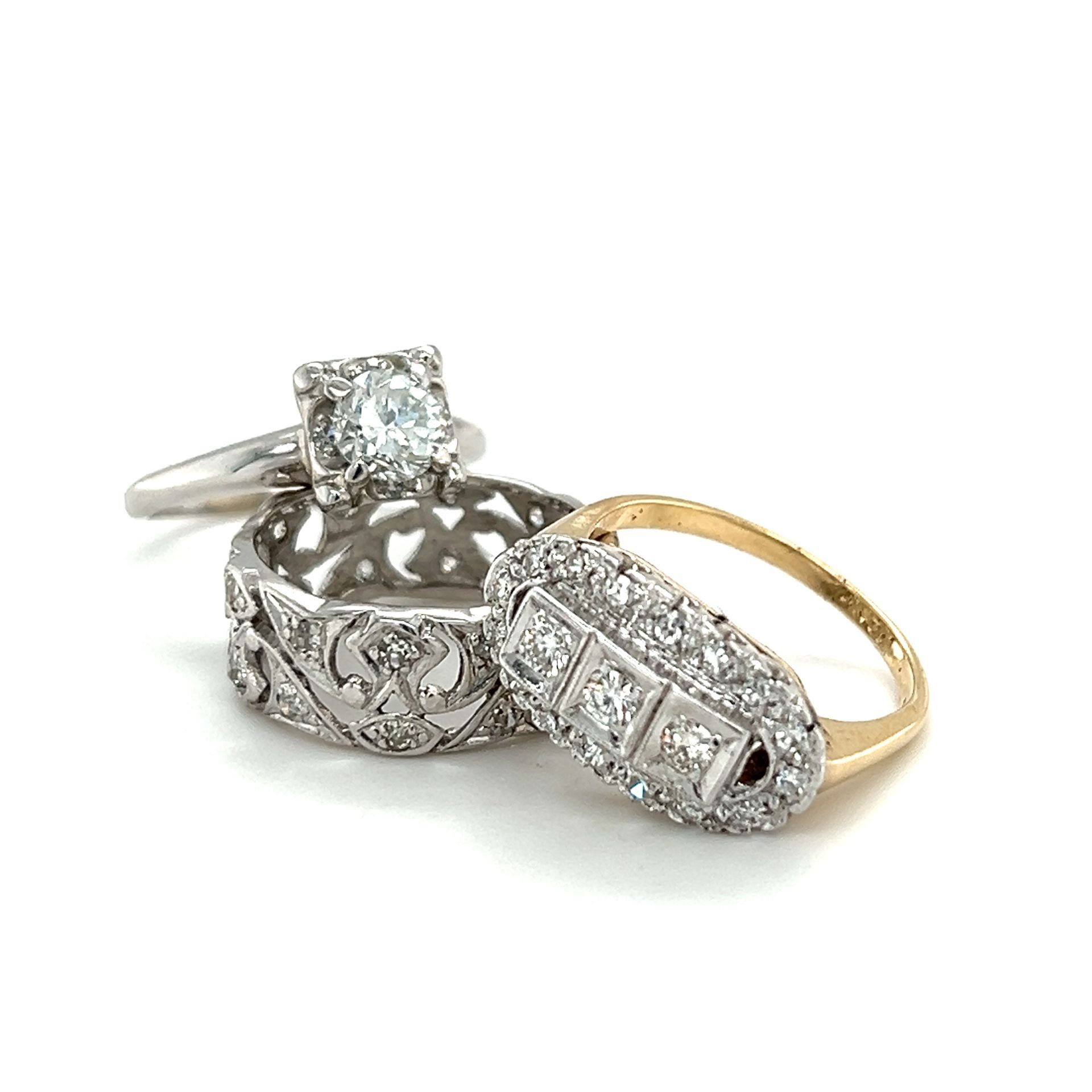 Three diamond rings on a white background: solitaire, filigree band, and a gold ring with a rectangular diamond cluster.