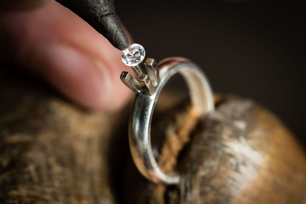 A jeweler setting a diamond in a silver ring with a handheld tool.