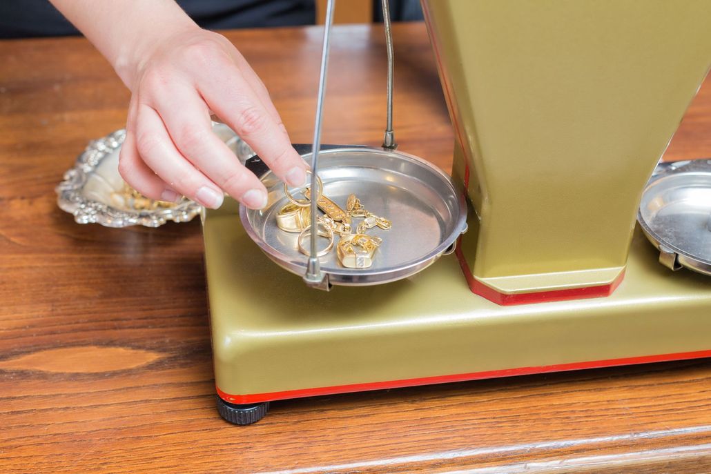 Hand placing gold pieces onto a balance scale's pan on a wooden table.