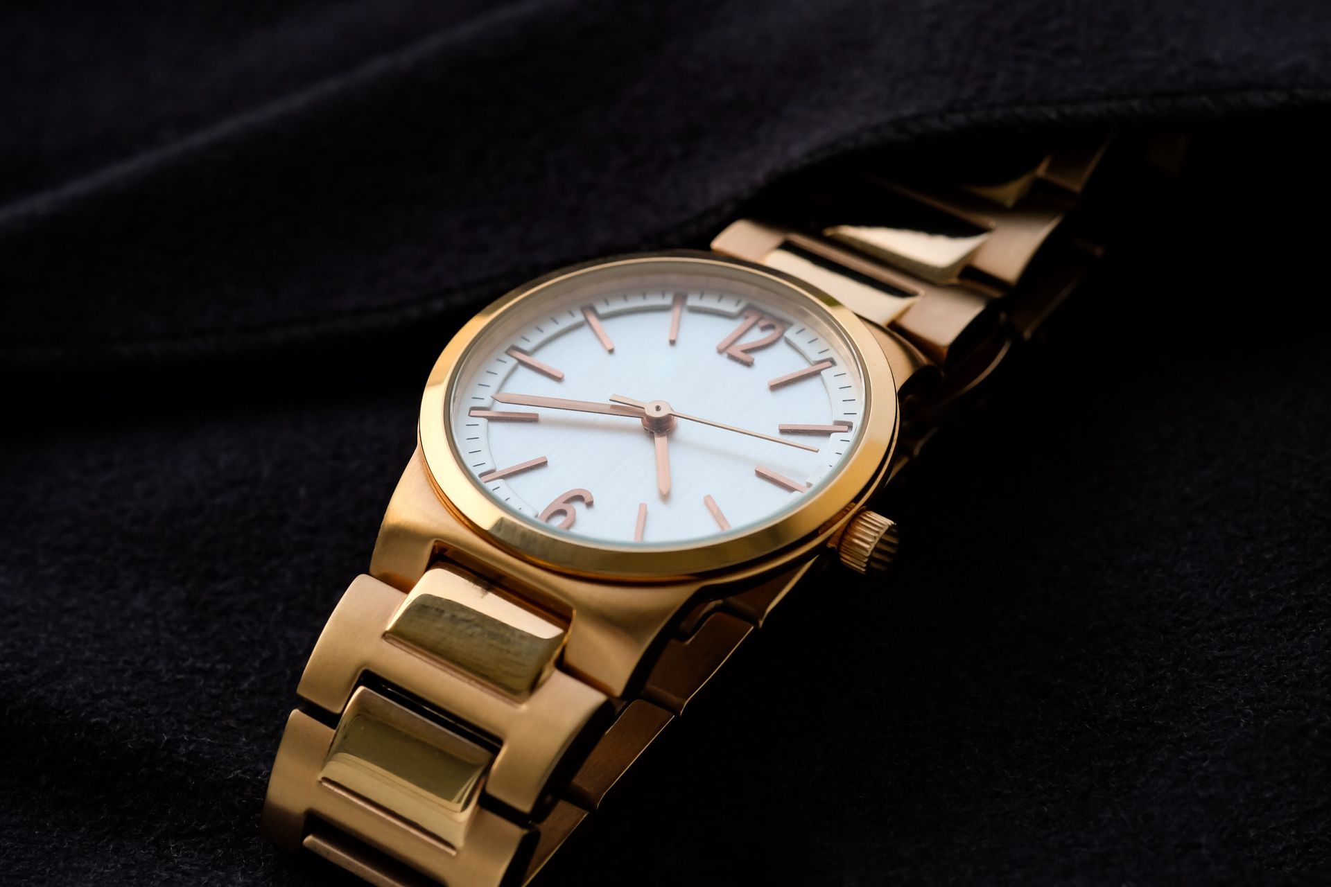 Gold wristwatch on a black fabric backdrop, showcasing the watch's face and metal band.