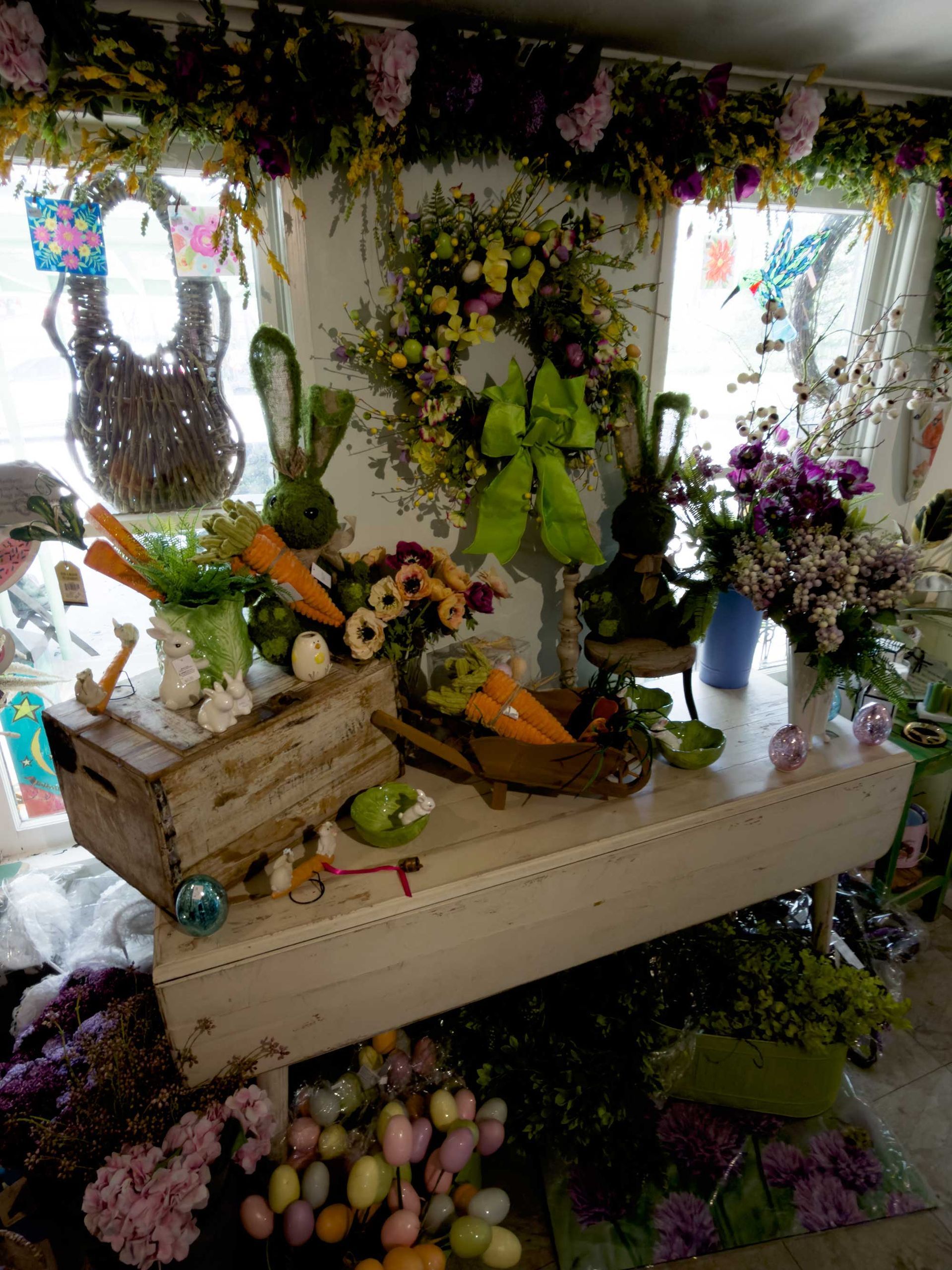 An Easter-themed table display with a wooden crate, artificial carrots, floral wreath, and colorful decorative eggs.