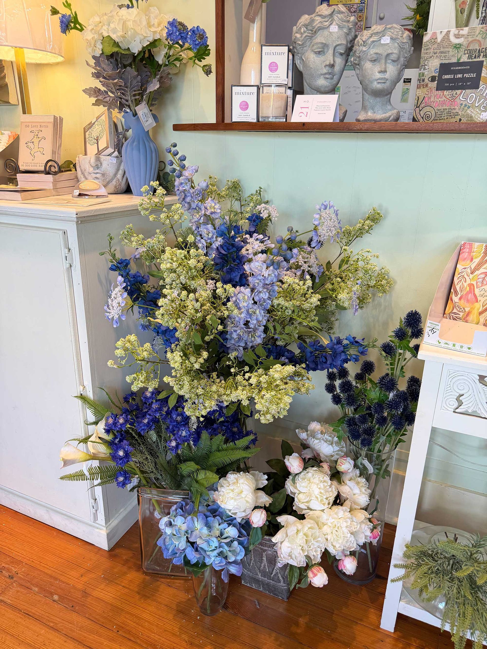 A floral display with blue delphiniums and white peonies arranged in glass vases inside a shop with light green walls.