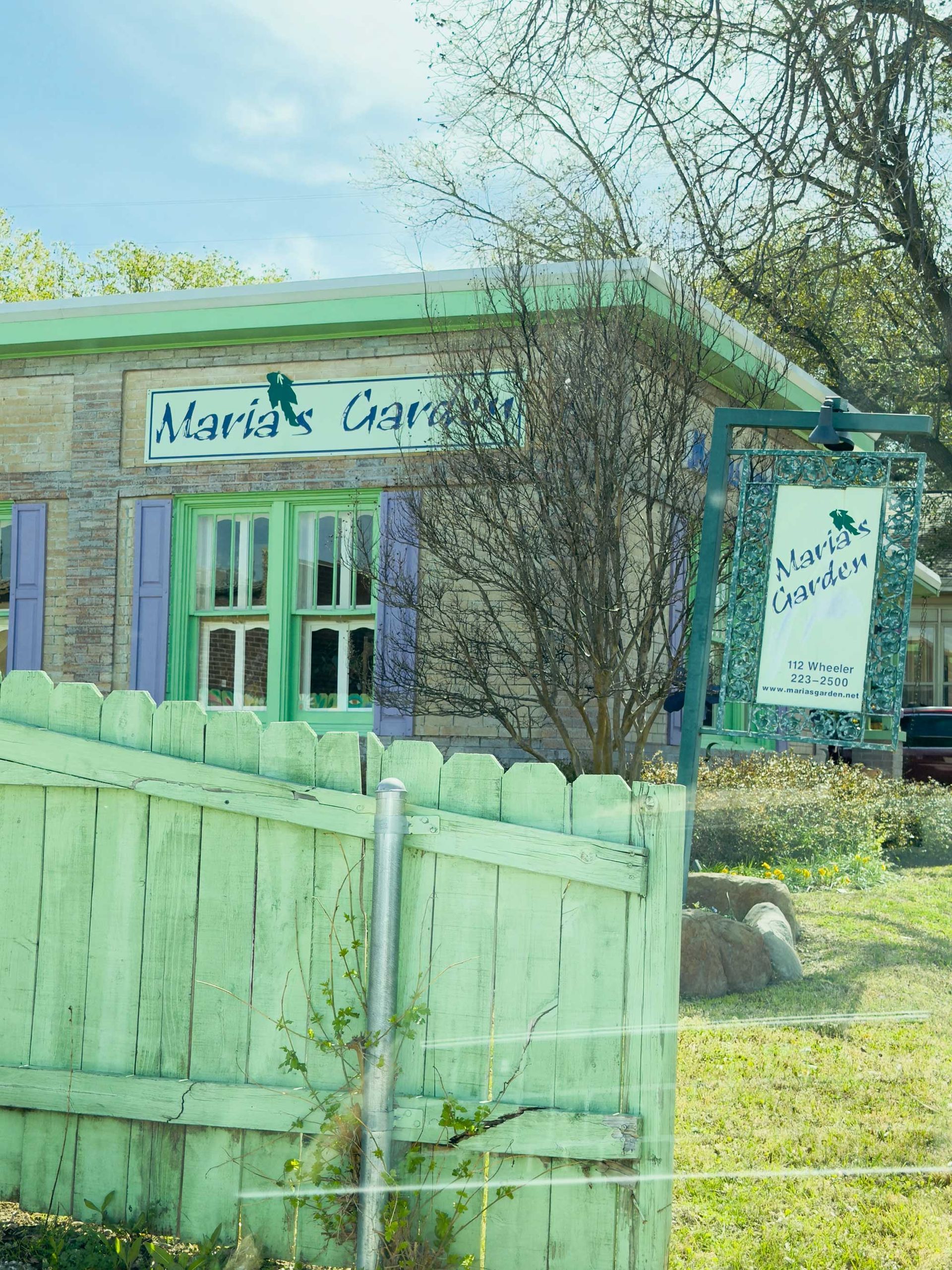 A pastel green picket fence frames a building with green trim and a matching hanging sign that reads 