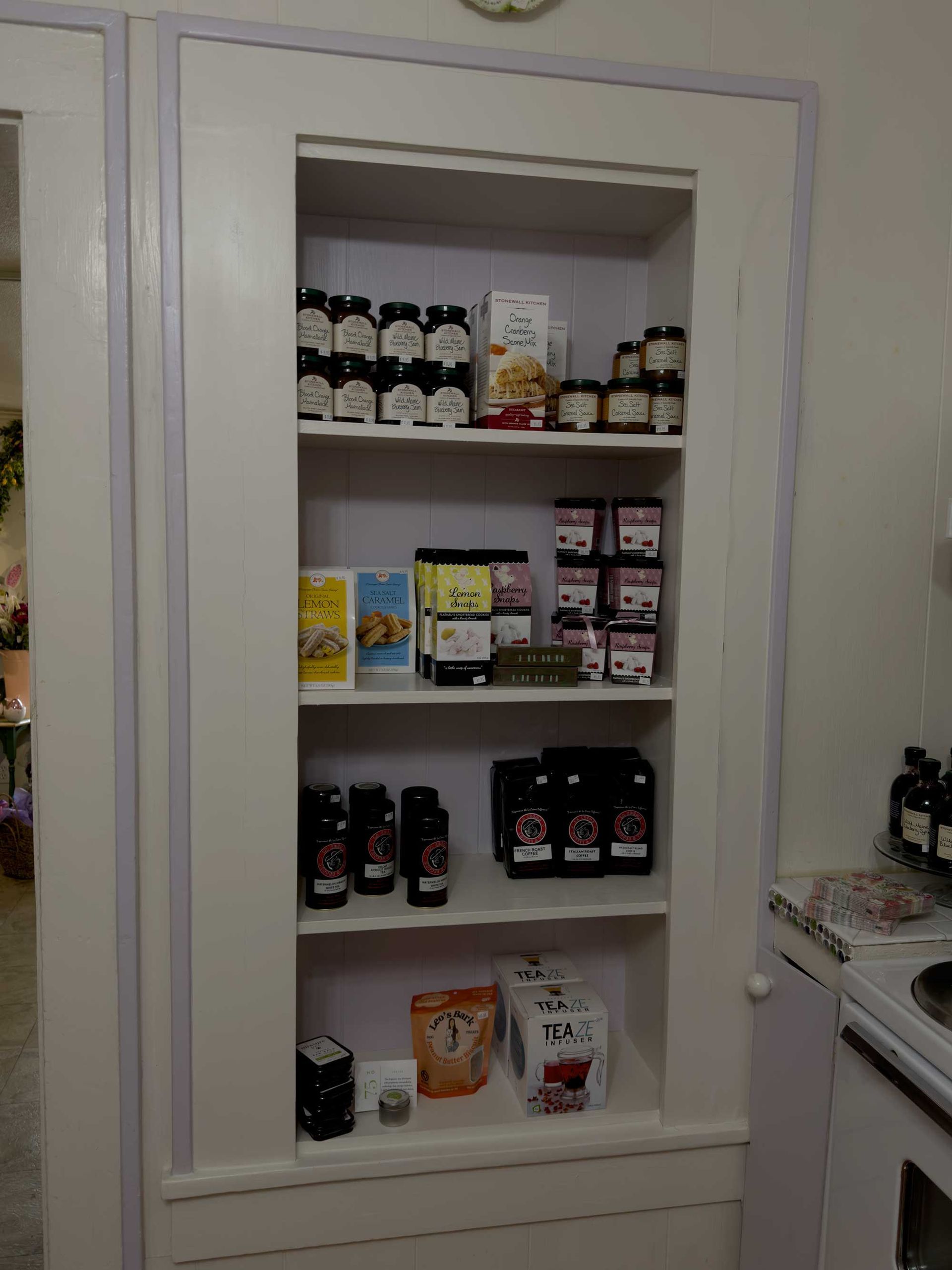 A white-framed built-in pantry with four shelves organized with various food items, jars, and boxed goods.