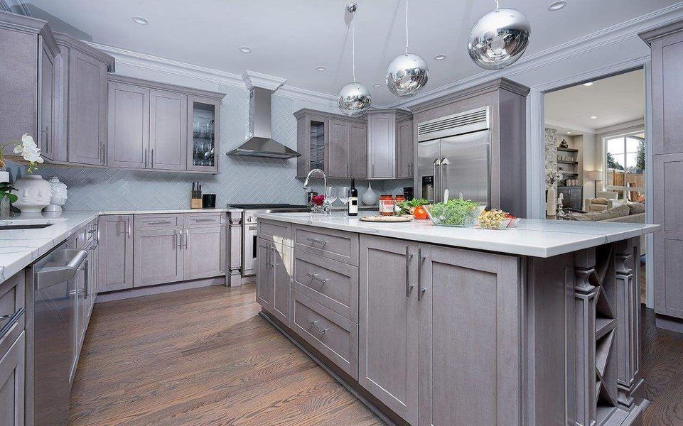 Gray kitchen with island, cabinets, and stainless steel appliances. Hardwood floors and decorative light fixtures.