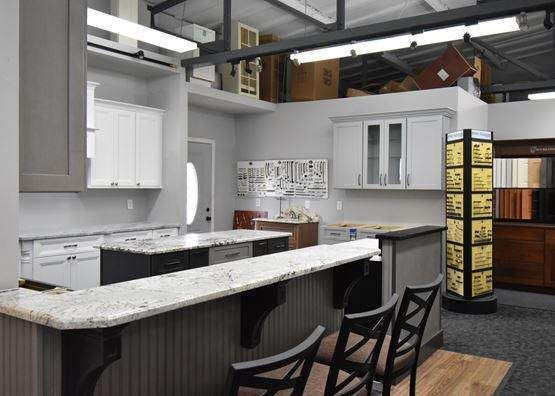 Kitchen showroom with gray and white cabinets, granite countertops, and bar stools.