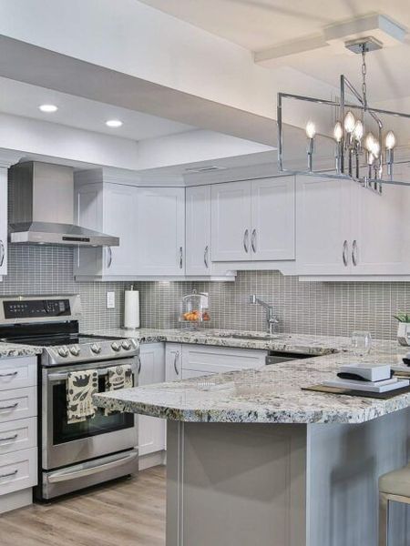 Modern white kitchen with stainless steel appliances, granite countertops, and a decorative light fixture.