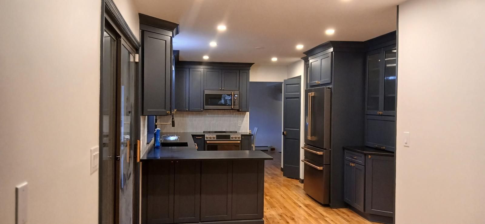 Dark kitchen with black cabinets, stainless steel appliances, and wood flooring.