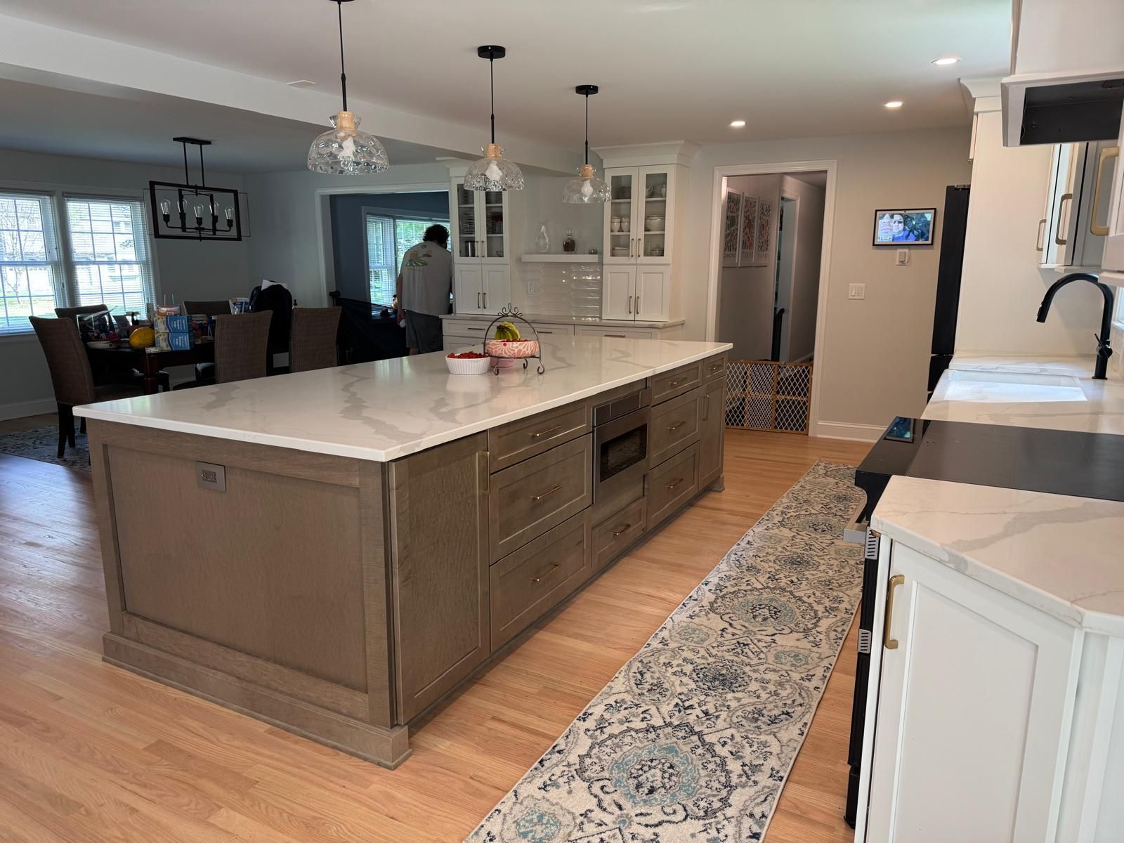 Kitchen with large island, wood cabinets, and marble countertops.  A person is visible.