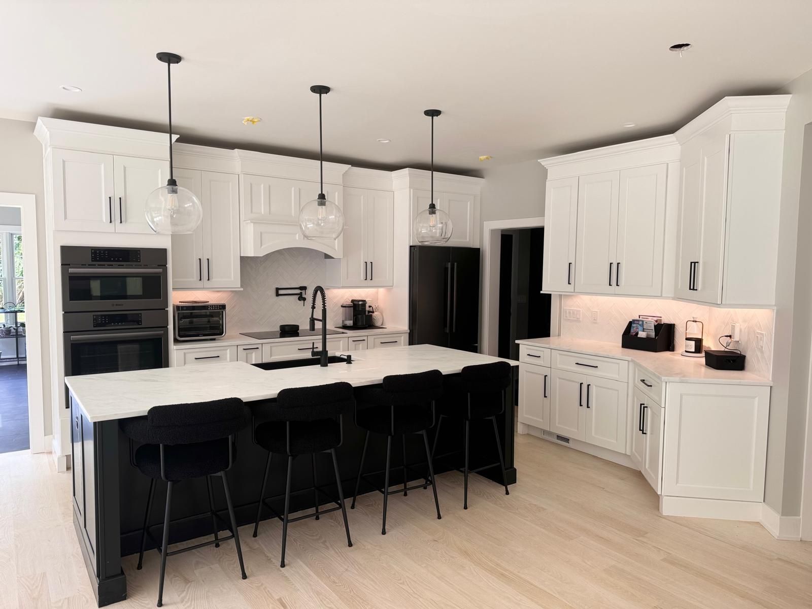 Modern kitchen with black island, white countertops and cabinets, pendant lights, and black stools.