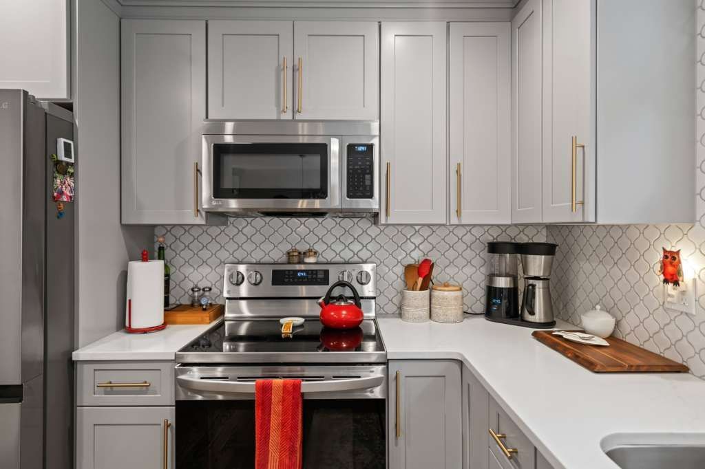 Grey and white kitchen with stainless steel appliances, white countertops, and gray cabinets.
