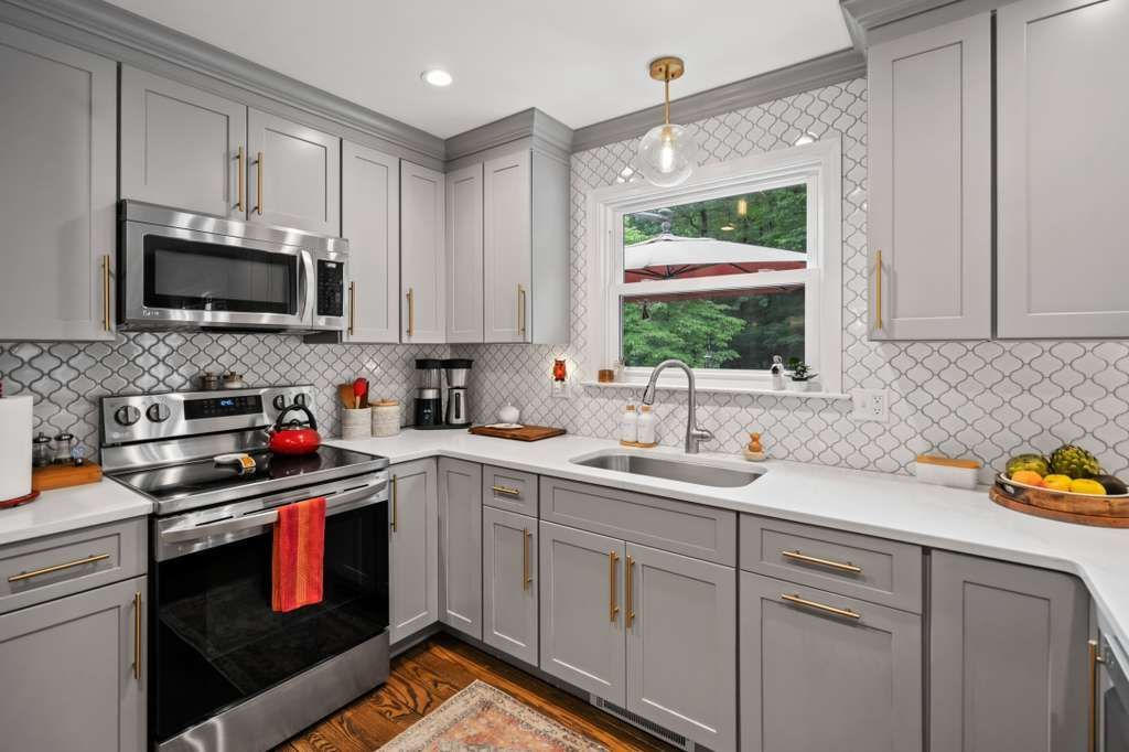 Gray kitchen with stainless steel appliances, white countertops, and gold hardware.