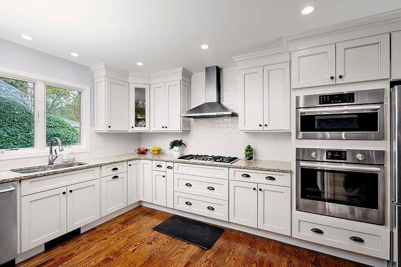 White kitchen with stainless steel appliances, white cabinets, granite countertops, and hardwood floors.