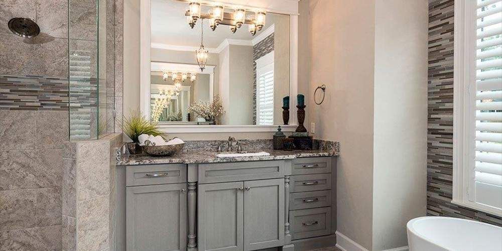 Bathroom with gray cabinets, granite countertop, and shower. Mirror, candles, and window with shutters.