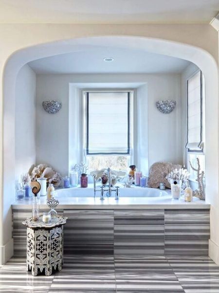 Bathroom with bathtub in an alcove, striped marble, arched opening, window, decorative objects.