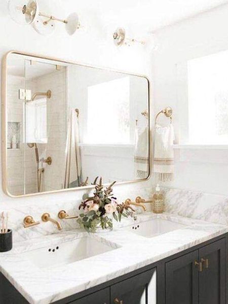 Bathroom with gold fixtures, marble countertop, black cabinets, rectangular mirror, and flower arrangement.