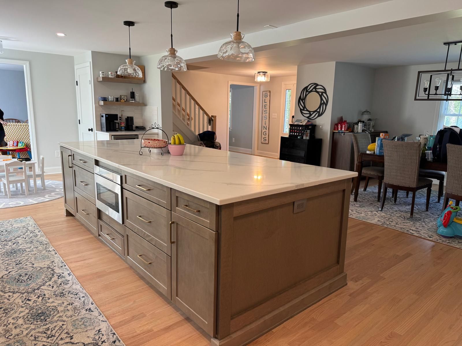 Spacious kitchen with large island, light cabinets, and wood flooring. Dining area and stairs are visible.