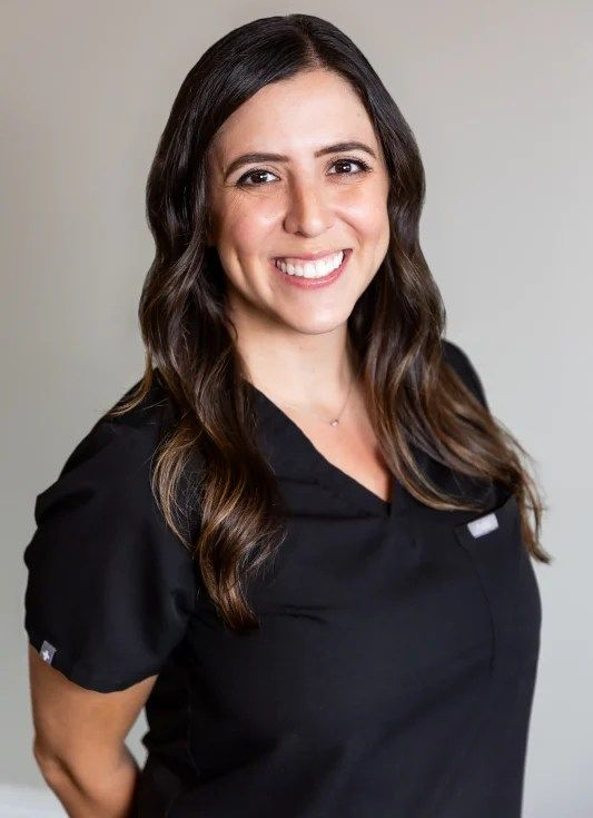 Woman in black scrubs smiles at the camera, against a light gray background.