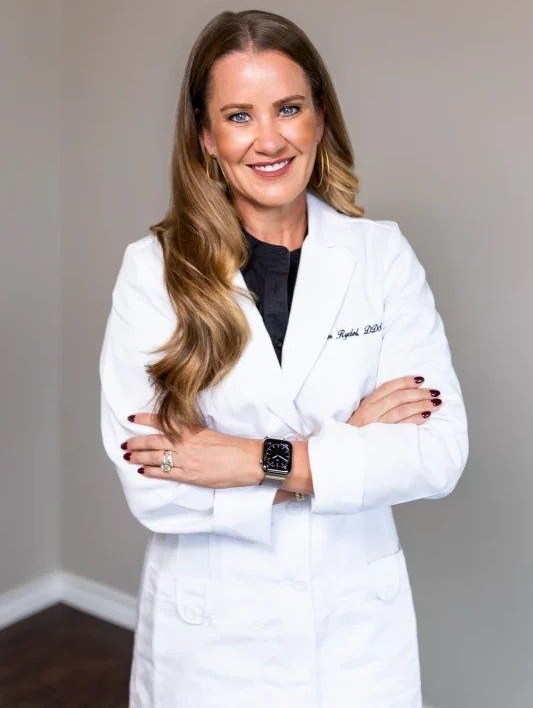 Woman in white lab coat with crossed arms, smiling.