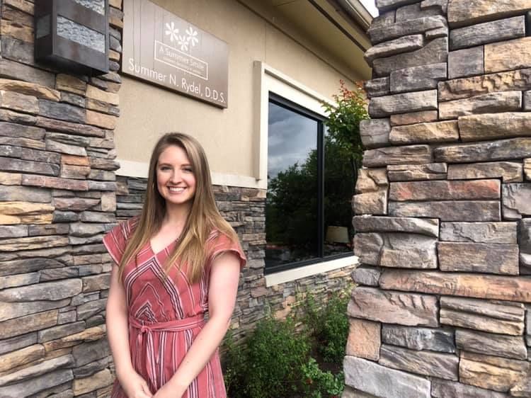 Woman in red striped dress smiles in front of a dental office with stone walls.