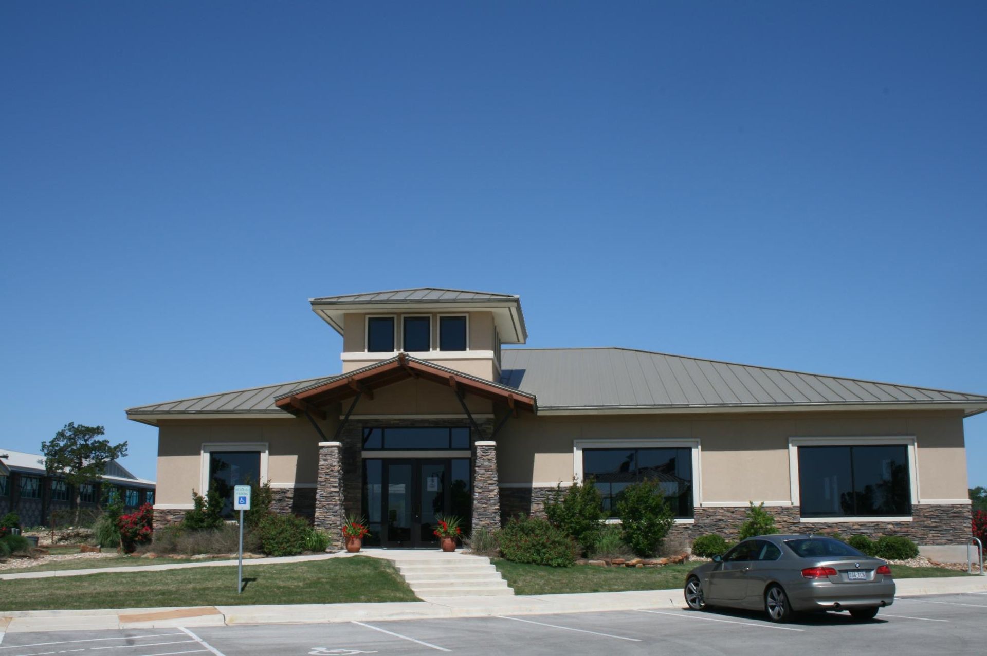 Tan stucco building with a stone entrance, blue sky, and a car in front.